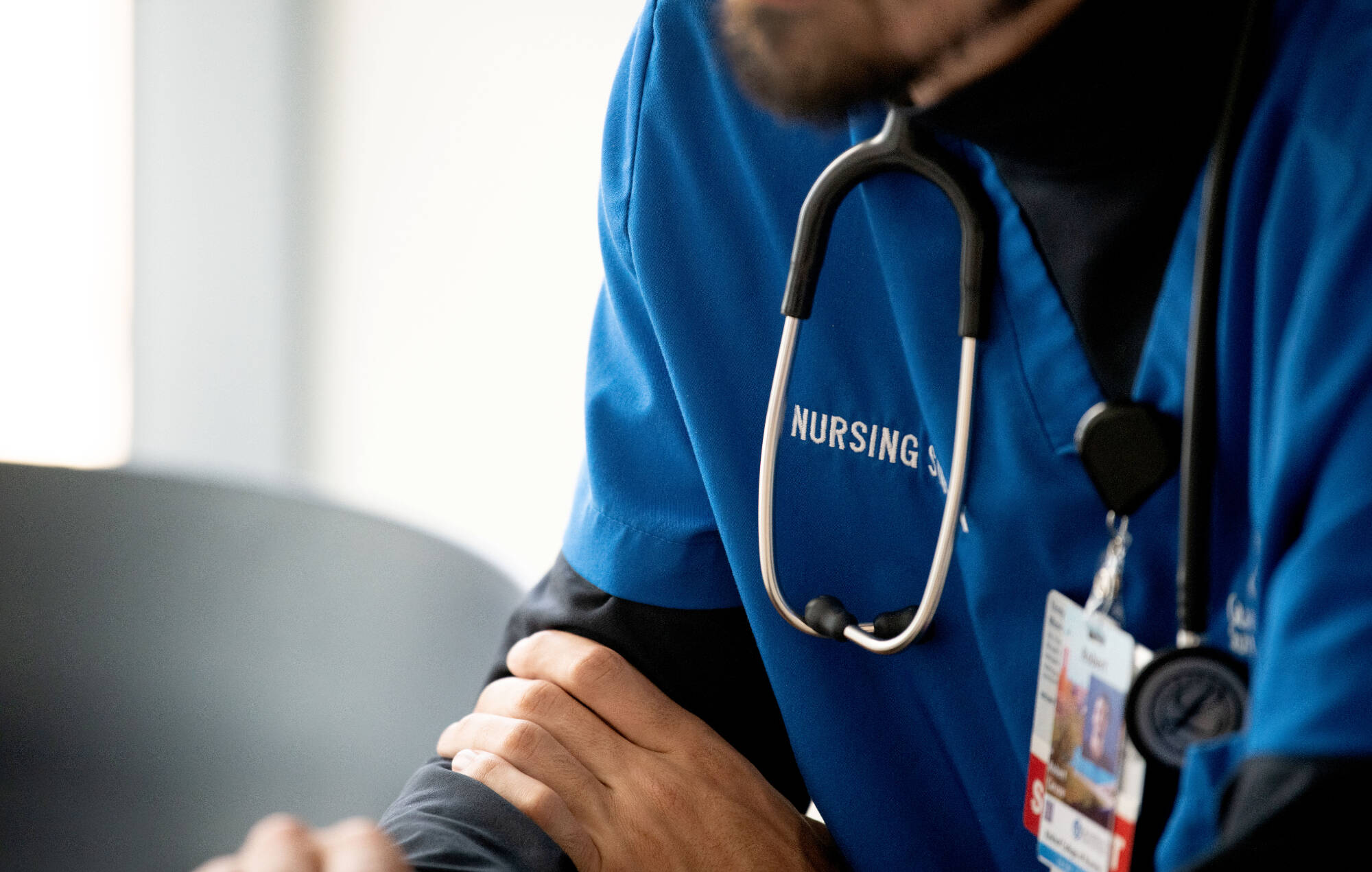 Student wearing a stethoscope, image focuses on the word "nursing" on the student's scrubs.